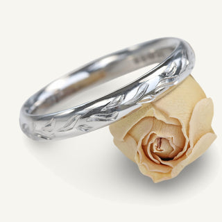 Platinum 3mm court wedding ring with hand engraved leaves, resting on a rose flower