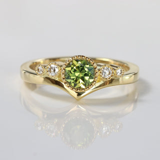 Handmade 18ct gold wishbone engagement ring with green sapphire and Canadian diamonds on reflective surface.