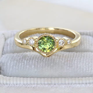 18ct gold wishbone engagement ring with green sapphire and diamonds photographed on pale fabric.