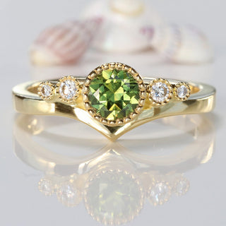 18ct gold green sapphire and diamond wishbone engagement ring on reflective surface