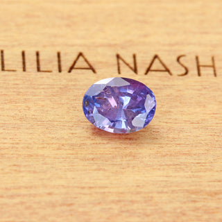 Natural oval purple sapphire displayed on Lilia Nash branded wooden background.