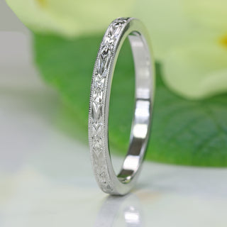 Platinum orange blossom engraved wedding ring photographed on green leaf with soft natural lighting.