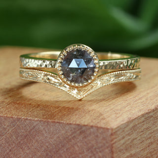 A gold wishbone ring shown with a salt and pepper diamond engagement ring placed on a wooden box