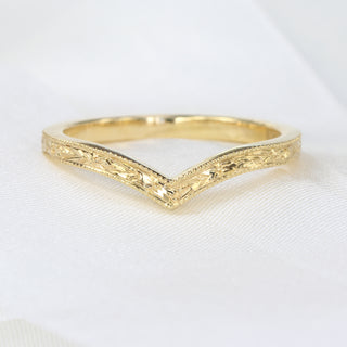 A gold wishbone ring with a textured surface shown on white fabric