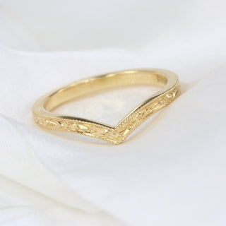 A gold wishbone ring with a textured surface shown on white fabric
