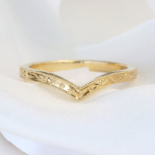 A gold wishbone wedding ring with an engraved orange blossom pattern on a white background.