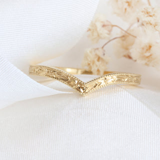 Gold wishbone ring with a textured design on a white fabric background