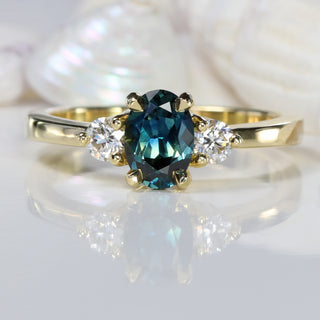 Teal sapphire and diamond trilogy engagement ring, with seashell background