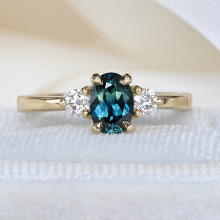 Parti sapphire trilogy engagement ring in handmade 18ct gold photographed on pale fabric.