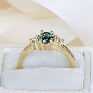 18ct gold trilogy engagement ring with natural Parti sapphire and diamonds photographed on pale fabric.