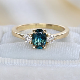 Parti sapphire trilogy engagement ring in handmade 18ct gold photographed on pale fabric.