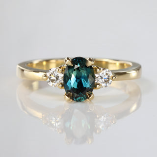 Handmade 18ct gold Parti sapphire trilogy engagement ring with Canadian diamonds on reflective surface.