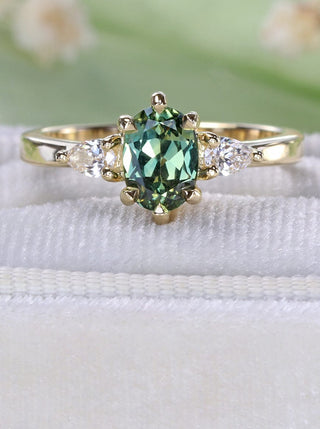 18ct gold three stone engagement ring with oval green sapphire and side diamonds on a velvet box with green background
