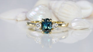 Teal sapphire and diamond trilogy engagement ring with seashell background