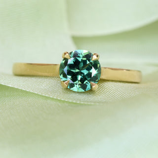 Handmade Parti sapphire solitaire engagement ring styled with soft green background.