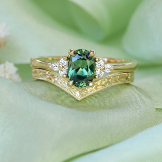 Oval Parti sapphire and diamond cluster engagement ring in handmade 18ct yellow gold and orange blossom engraved wishbone wedding ring, photographed on green satin.