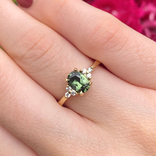 Oval Parti sapphire and diamond cluster engagement ring in handmade 18ct yellow gold shown on hand.