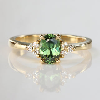 Handmade 18ct yellow gold engagement ring with a natural unheated oval Parti sapphire and Canadian diamond cluster, photographed on a reflective surface.