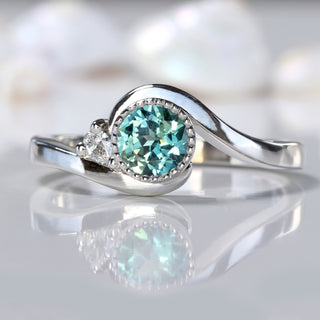 Close up of Parti sapphire platinum wave engagement ring on reflective background with shells