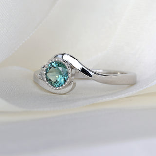 Platinum wave engagement ring with teal Parti sapphire and diamond accent showing flowing band shape.