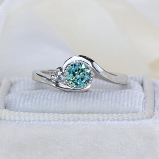 Natural unheated teal Parti sapphire in platinum wave setting with pear cut diamond accent.