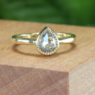 Handmade 18ct gold pear cut salt and pepper diamond engagement ring on wooden surface.
