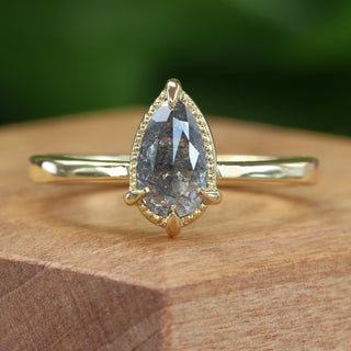 Close up of pear cut salt and pepper diamond engagement ring on wooden background.