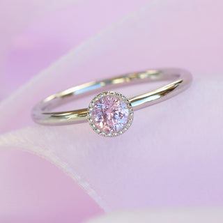Petite platinum pink sapphire solitaire ring photographed on soft pink fabric.
