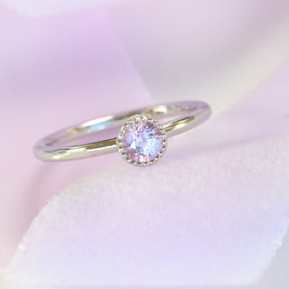 Angled view of platinum solitaire ring set with a pink sapphire on pink silk