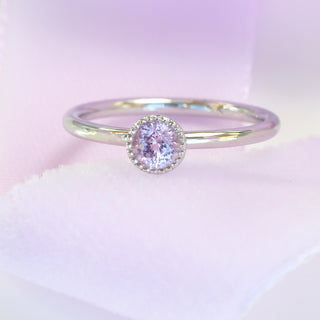 Close-up of platinum pink sapphire solitaire ring on pale pink fabric.