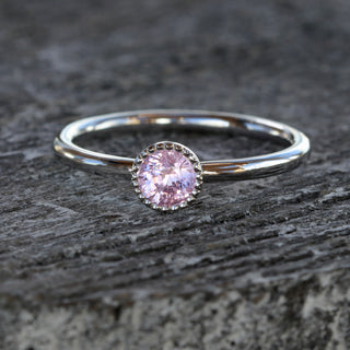 Pink sapphire solitaire ring in platinum photographed on grey texture.
