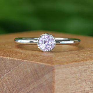 Handmade platinum pink sapphire solitaire engagement ring with milgrain bezel on wooden block.