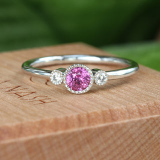 Petite pink sapphire and diamond trilogy engagement ring on a wooden box.