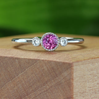 Patinum trilogy engagement ring with pink sapphire photographed against green background