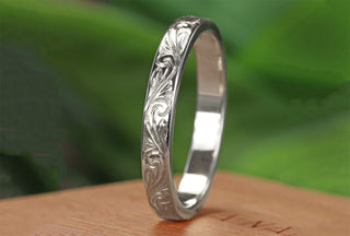 Angled view of Platinum wedding band engraved with a floral scroll pattern on a wooden box with blurred green background