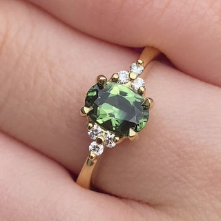 Handmade Oval Parti sapphire and diamond cluster engagement ring in 18ct yellow gold shown on hand.