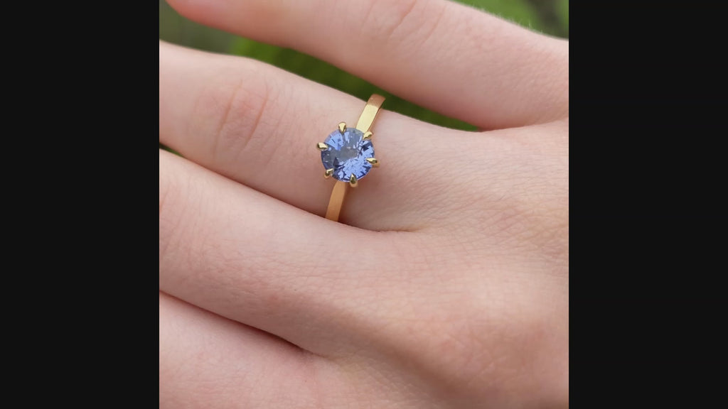 18ct gold lavender sapphire solitaire engagement ring shown worn outdoors.
