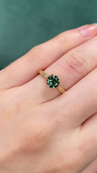 Video of a green sapphire 18ct gold solitaire engagement ring with floral engraved detail being worn on the hand
