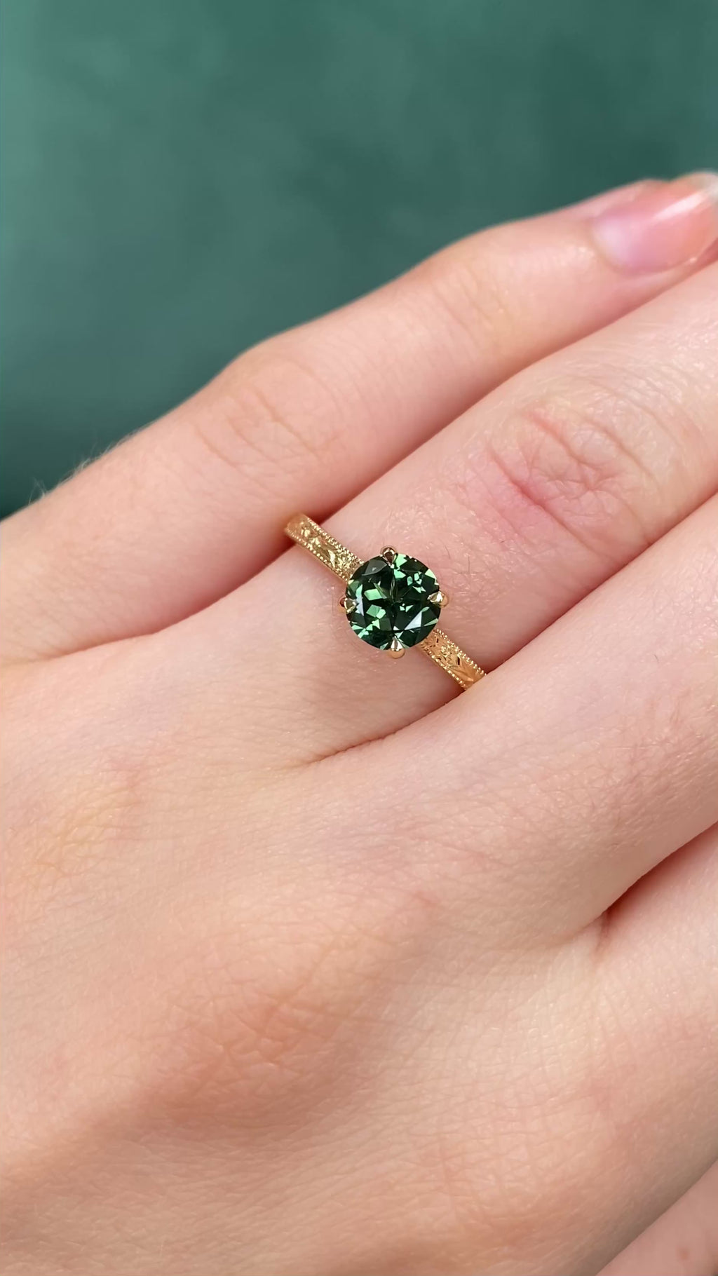 Video of a green sapphire 18ct gold solitaire engagement ring with floral engraved detail being worn on the hand