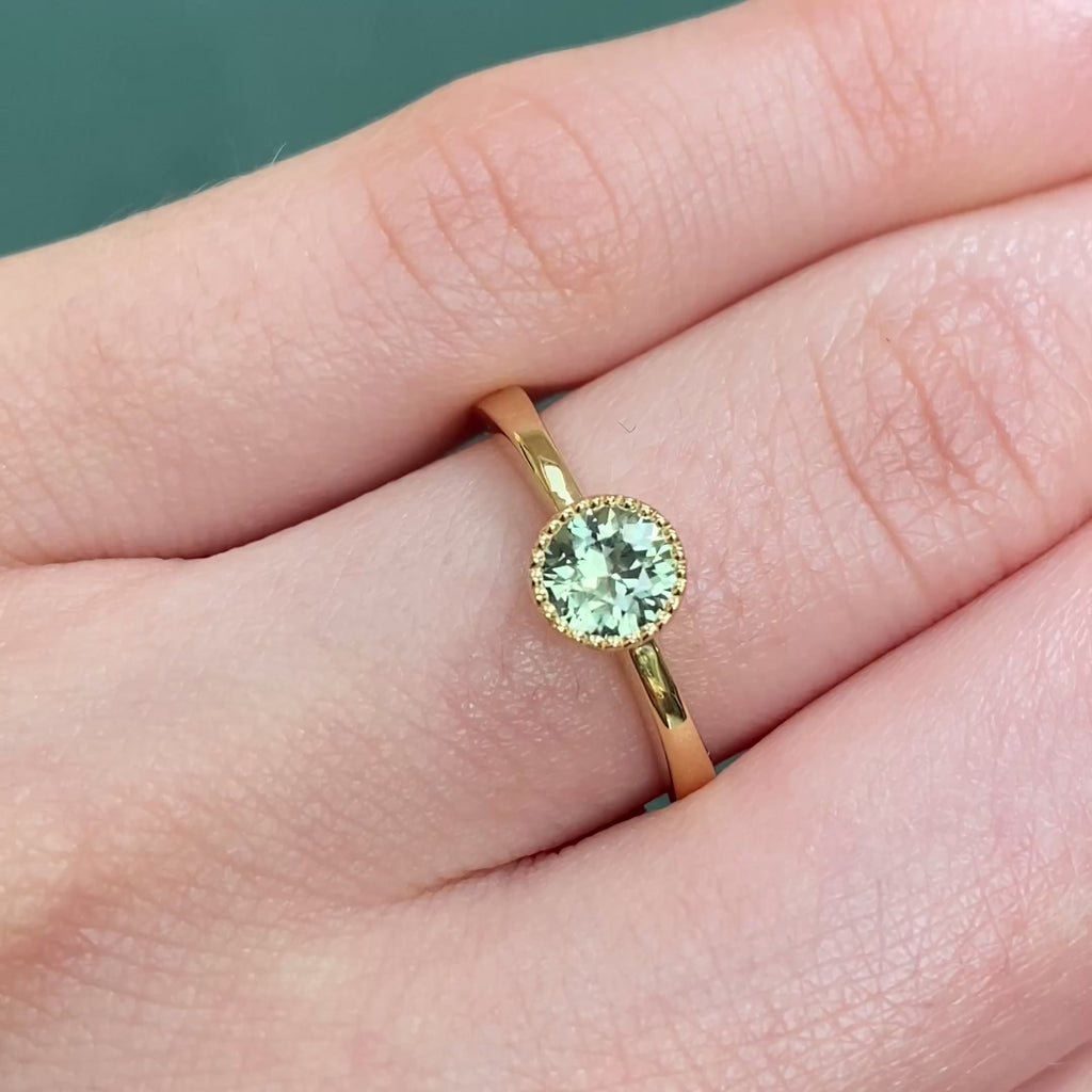 Green sapphire solitaire engagement ring in 18ct gold shown worn on hand.