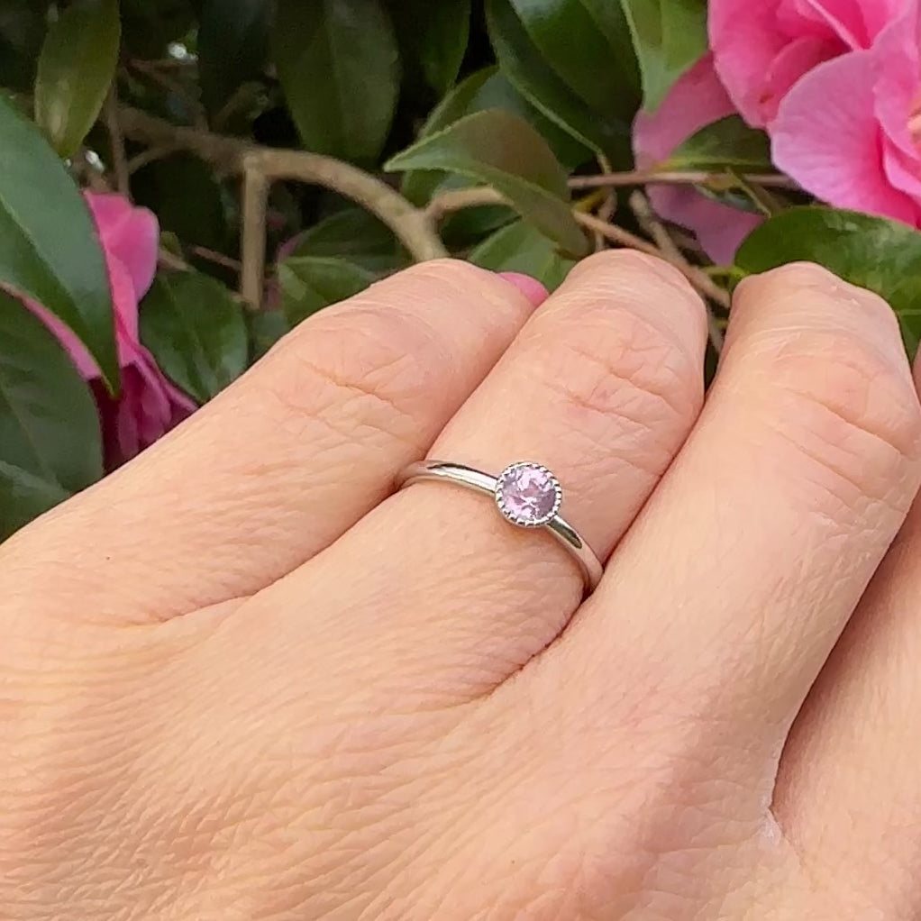 Petite pink sapphire solitaire engagement ring shown worn on hand in natural light.