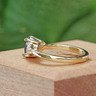 Oval purple sapphire engagement ring with pear cut diamonds photographed at an angle.