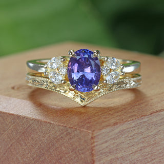 Handmade oval purple sapphire and diamond cluster ring with fitted wishbone wedding ring on a wooden ring box.