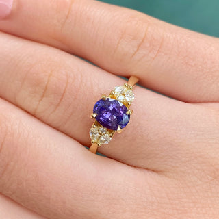 Oval purple sapphire and diamond engagement ring shown worn on hand.