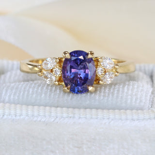 18ct gold oval purple sapphire engagement ring photographed on pale textured fabric.