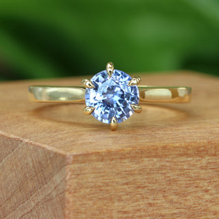 Lavender blue sapphire solitaire engagement ring photographed on wooden surface.