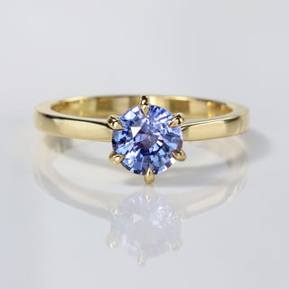 Handmade 18ct gold lavender blue sapphire solitaire engagement ring on reflective surface.