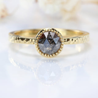 Close-up of 18ct gold salt and pepper diamond solitaire ring on pale background.
