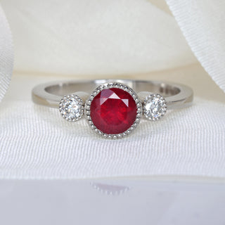 Natural red ruby and diamond trilogy engagement ring on white silk ribbon