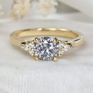 18ct gold cluster engagement ring with salt and pepper diamond photographed on pale fabric.